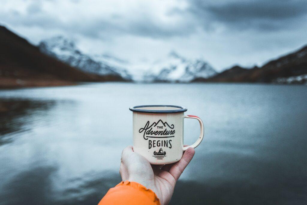 Jemand hält eine Tasse vor einem See